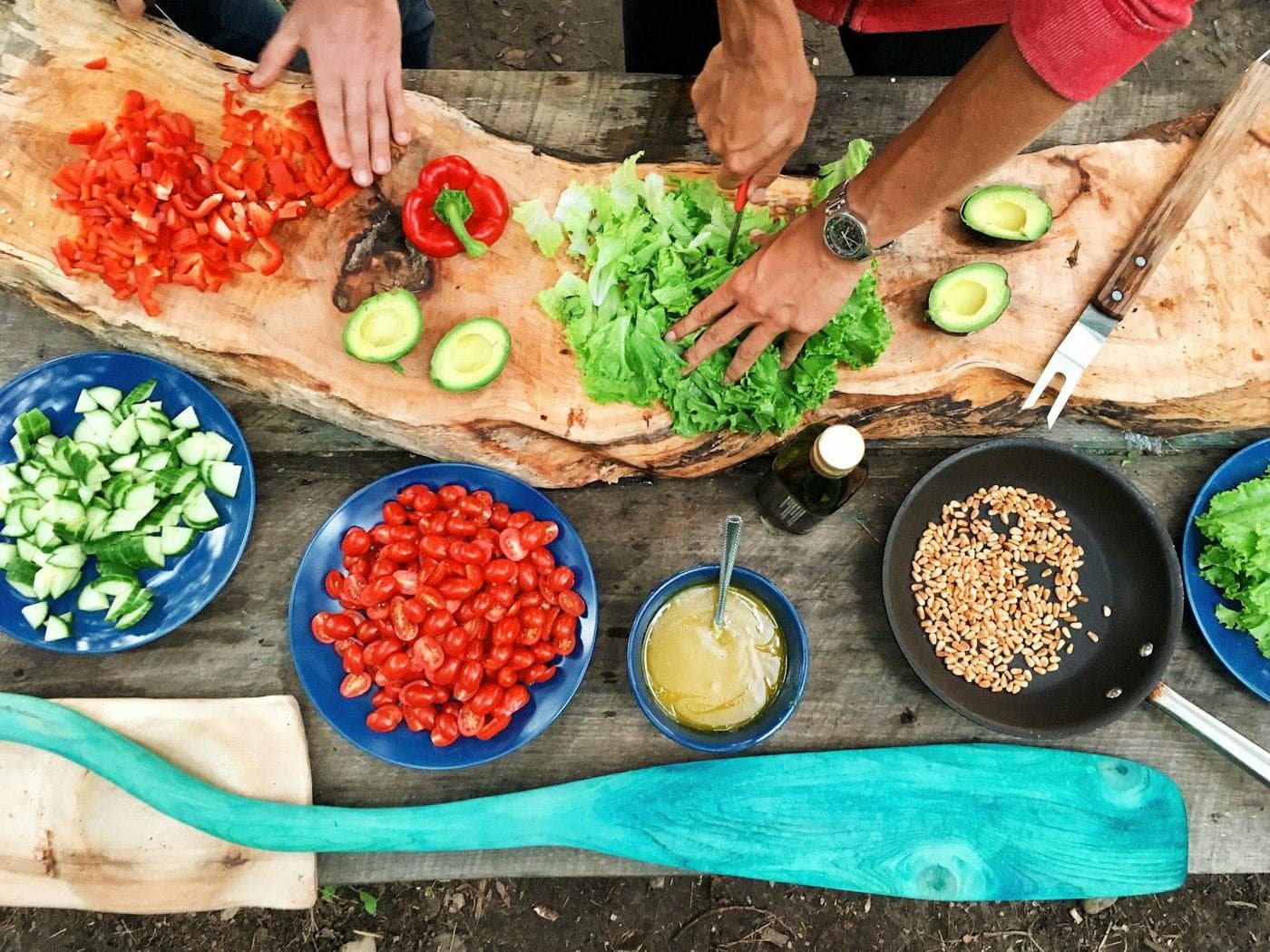 Mains préparant des légumes sur une planche, plats autour